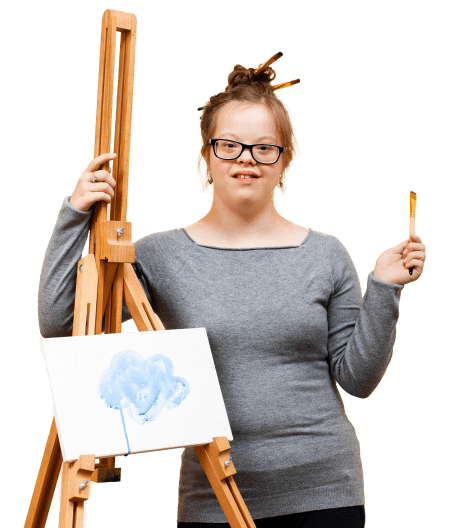 Student in a grey shirt smiles by an easel with artwork on it.